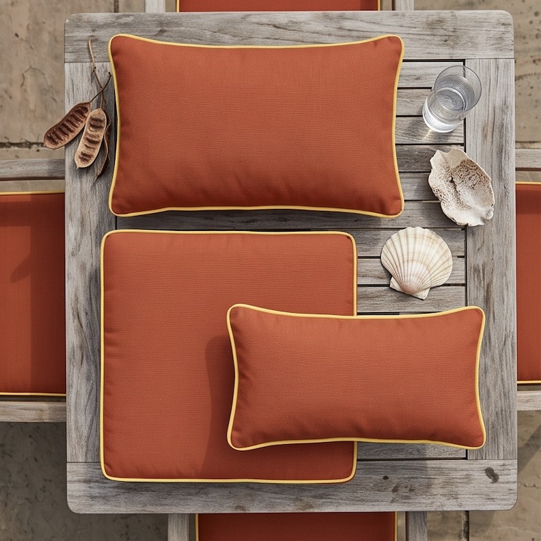 Cushiere cushions in Canvas Terracotta and Canvas Buttercup arranged on a teak table with seashells
