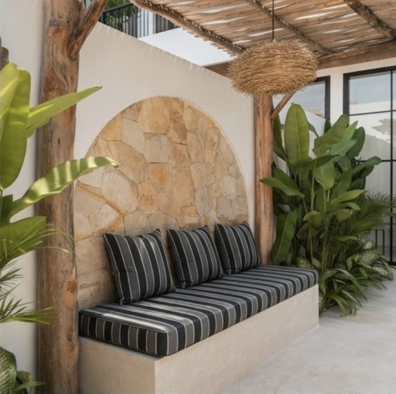 A stone-clad daybed bench with a charcoal and cream striped cushion, set beneath a woven pergola